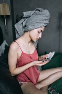 A woman in casual attire enjoys a skincare moment indoors with natural light.
